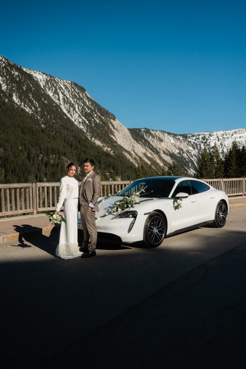Les mariés devant la Porsche Taycan, face aux Alpes