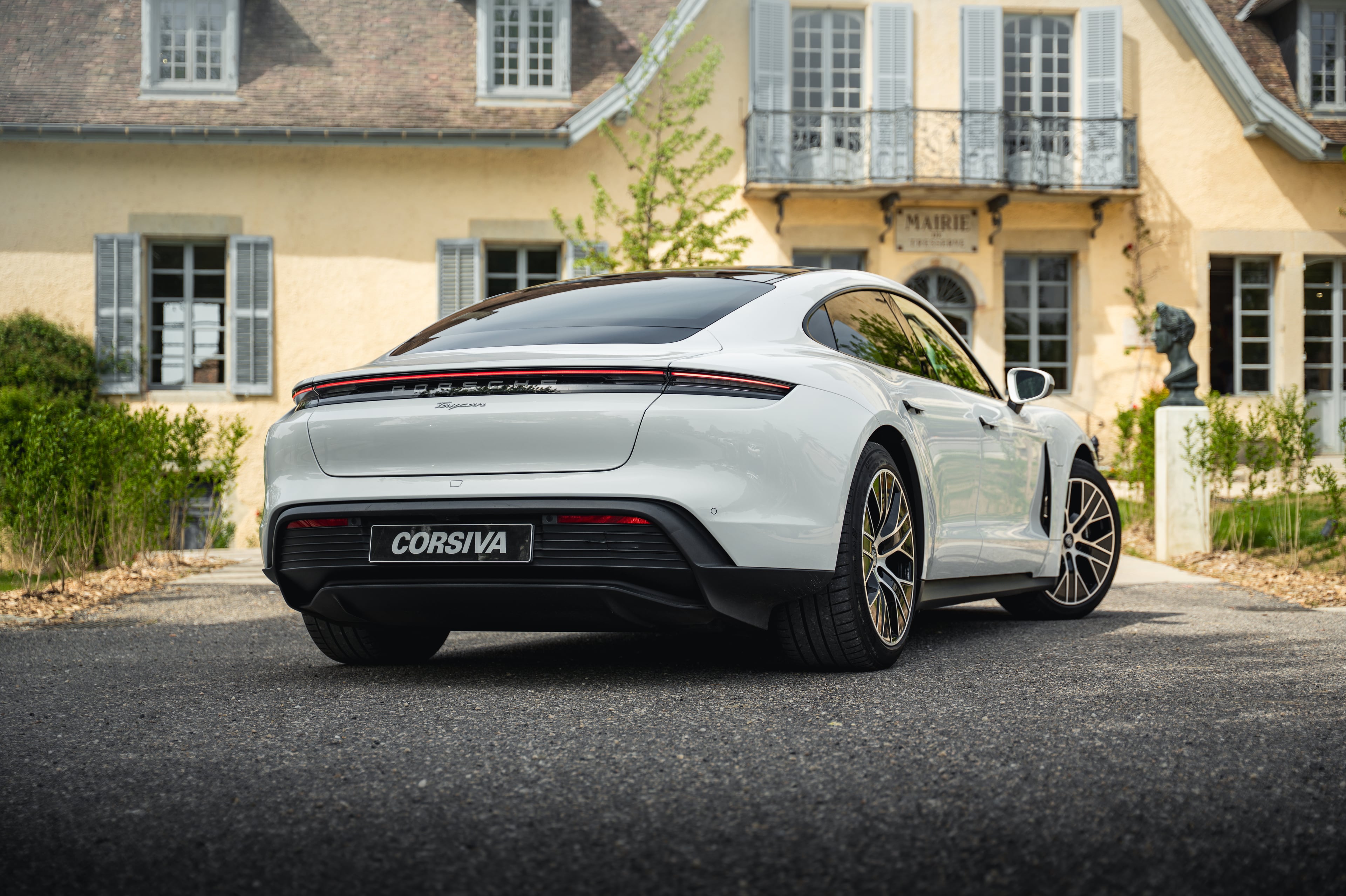 Porsche Taycan blanche de trois quarts arrière devant une demeure de caractère